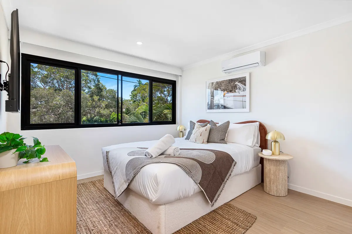 Queen bed beside a black-framed window in a studio