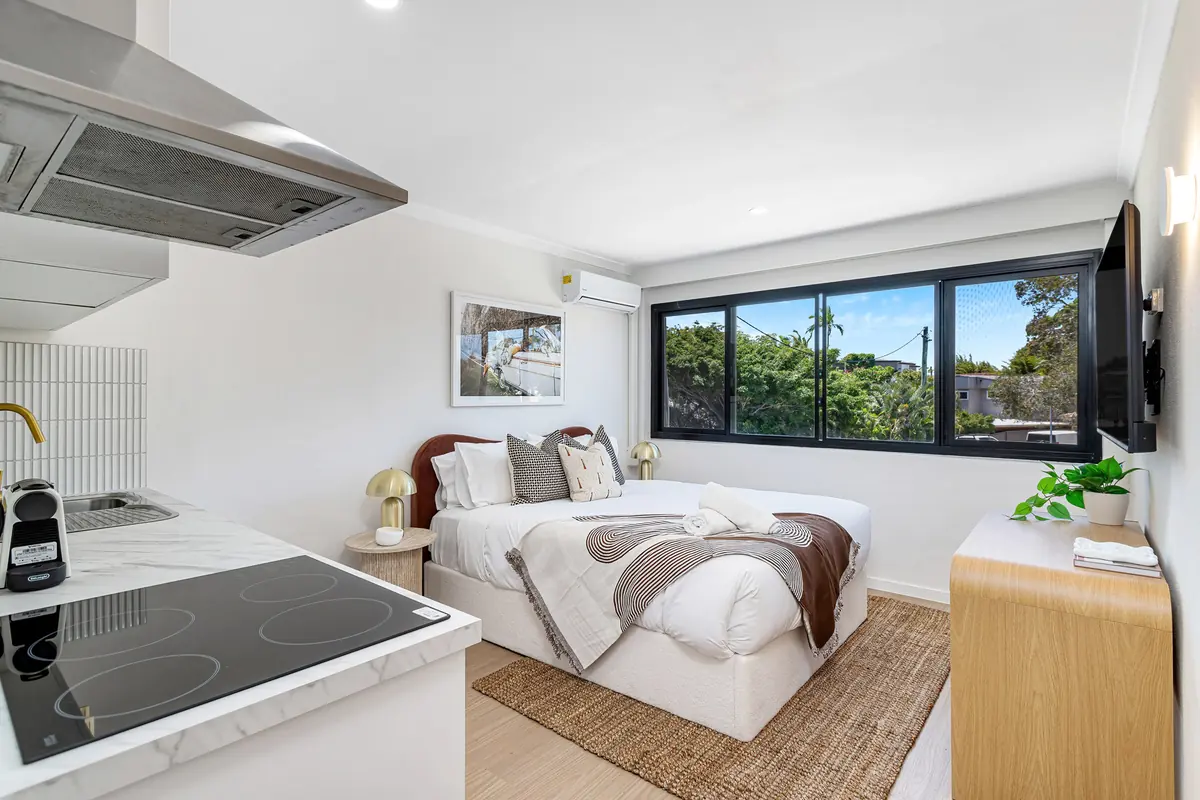 Studio kitchenette with a cooktop and rangehood beside the bed